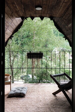Una habitación acogedora con techo de madera, cerca metálica, un banco acolchado y vistas a un bosque verde exuberante.