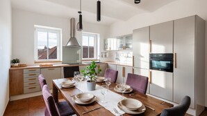 A modern kitchen with a dining table set for four, featuring a potted plant, wine glasses, and a built-in oven.