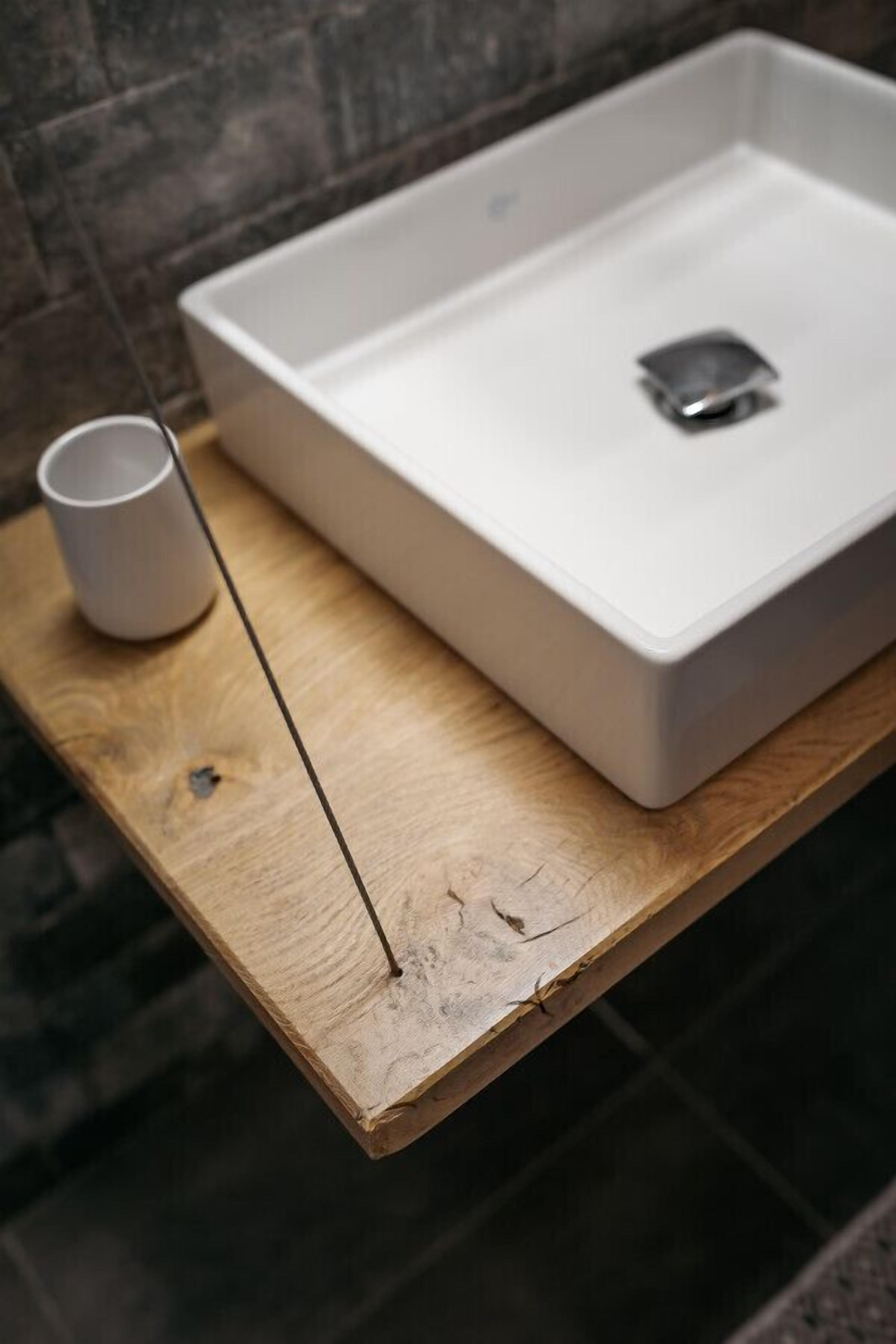 Un baño con un lavamanos blanco, una bandeja de madera y una taza blanca.