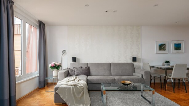 A modern living room with a grey sofa, a glass coffee table, and a grey rug.