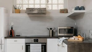 A modern kitchen with white cabinets, a built-in oven, a microwave, and a hanging pendant light.