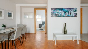 A modern living room with a dining area, a painting on the wall, and a white bench with a vase.