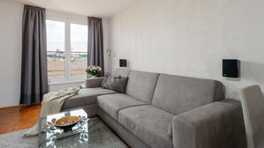 A modern living room with a grey sofa, a glass coffee table, and a view of a cityscape through large windows.