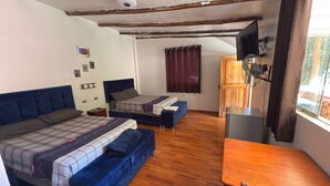 Une chambre avec deux lits, une table en bois, un téléviseur et une fenêtre avec des rideaux.