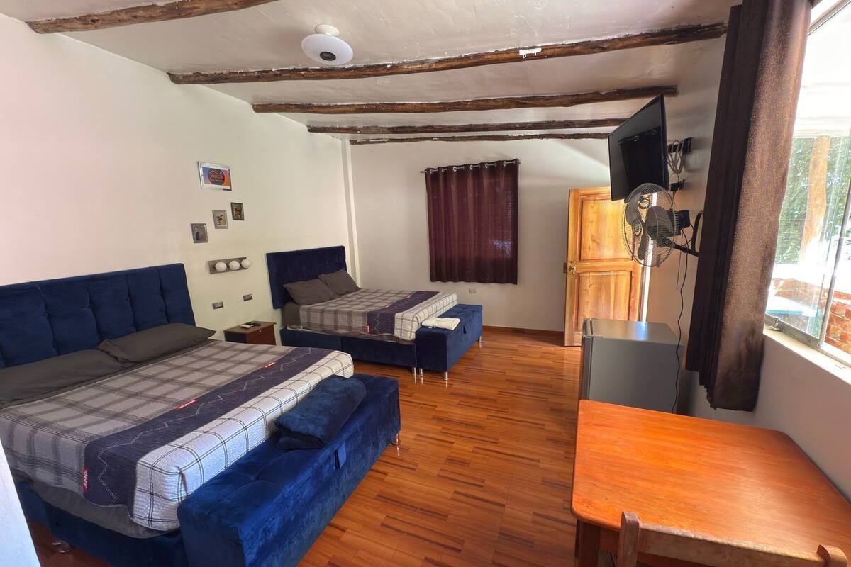 Une chambre avec deux lits, une table en bois, un téléviseur et une fenêtre avec des rideaux.