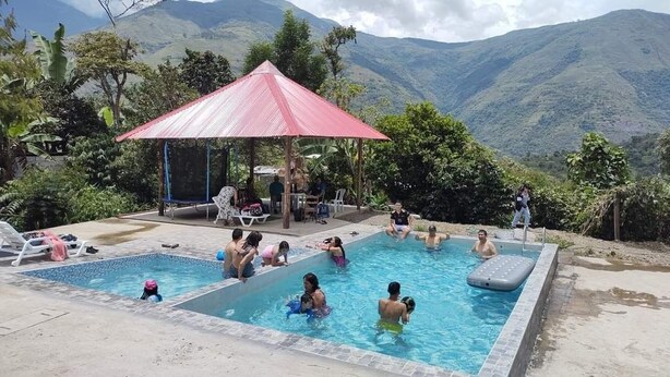 Un espace piscine agrémenté d’un pavillon au toit rouge, entouré d’une végétation luxuriante et avec des montagnes en toile de fond.