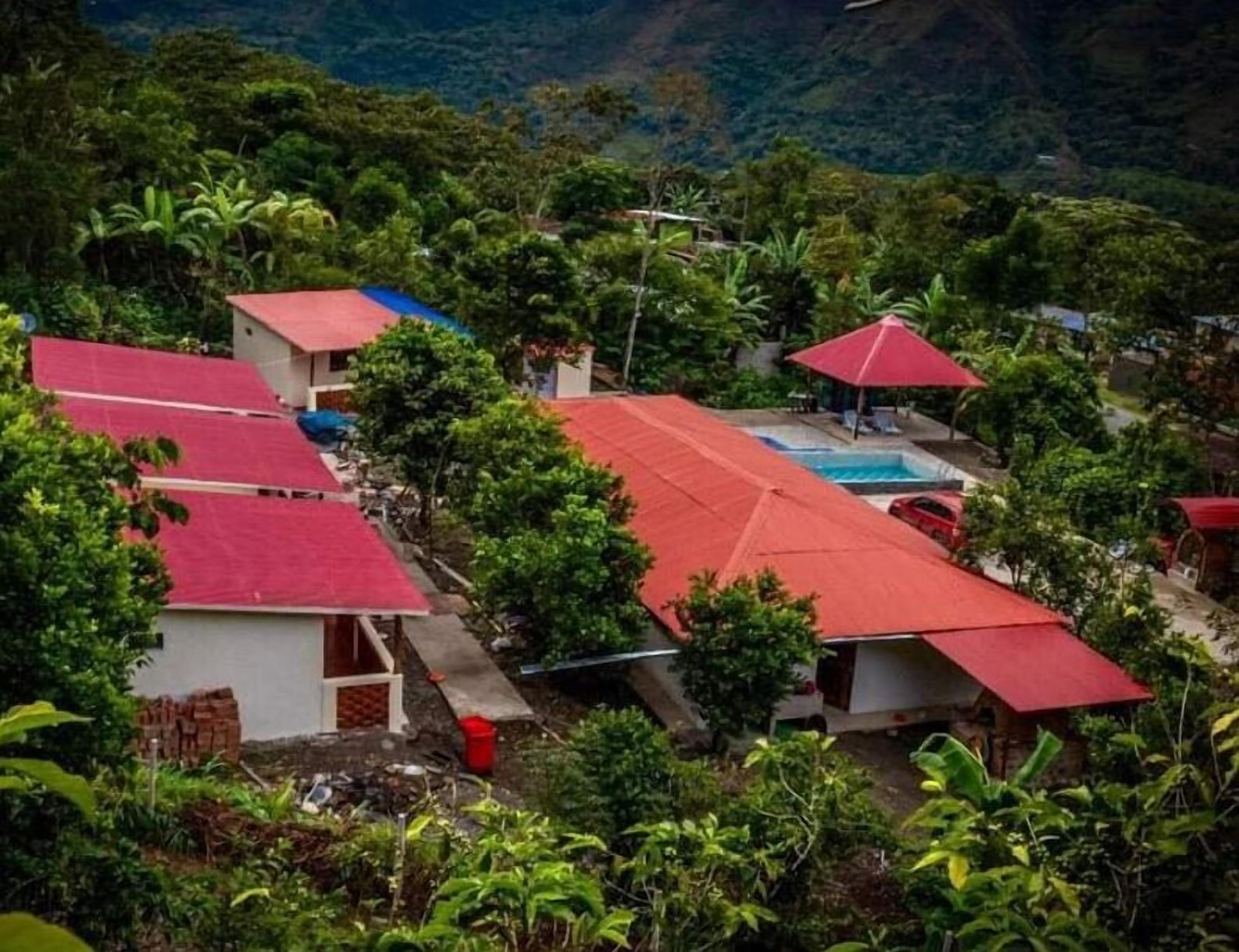A hillside property with multiple red-roofed buildings, a swimming pool, and lush greenery.