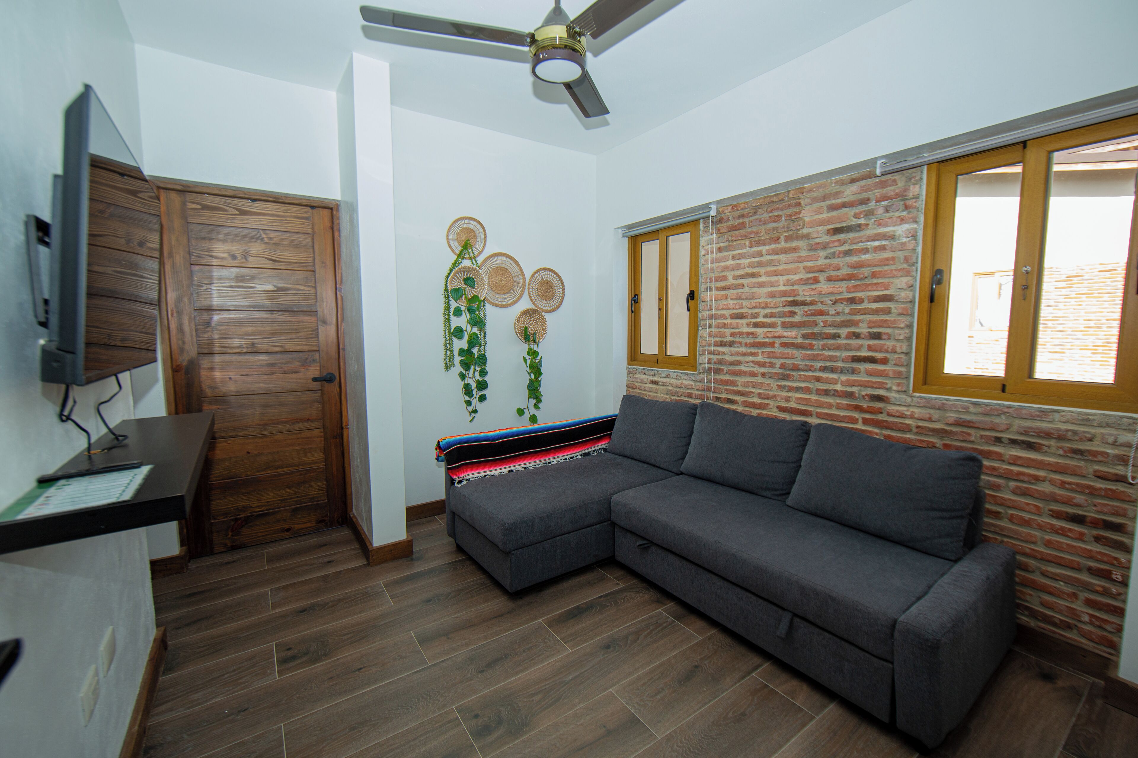 A modern living room with a sectional sofa, a wooden door, a brick wall, and a ceiling fan.