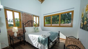 A bedroom with a bed, a nightstand, a lamp, and a wicker chair.