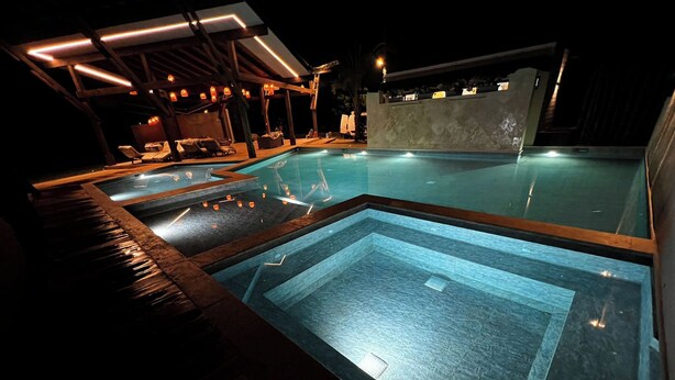 A pool area with multiple pools, lounge chairs, and a covered seating area with ambient lighting.