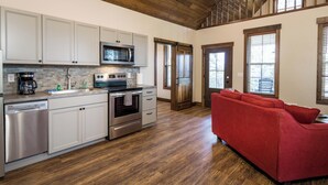 A kitchen with stainless steel appliances, a dishwasher, and a red sofa in a spacious living area with wooden flooring and a high ceiling.