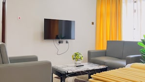 Una sala de estar moderna con un televisor de pantalla plana, sofás grises, una mesa de centro de mármol y una cortina amarilla.