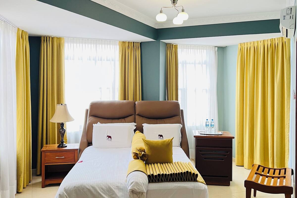 A hotel room with a large bed, two bedside tables, a chair, and a window with curtains.