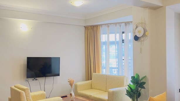 Habitación de hotel con una cama, dos sofás, una mesa de centro, un televisor y una ventana con cortinas.