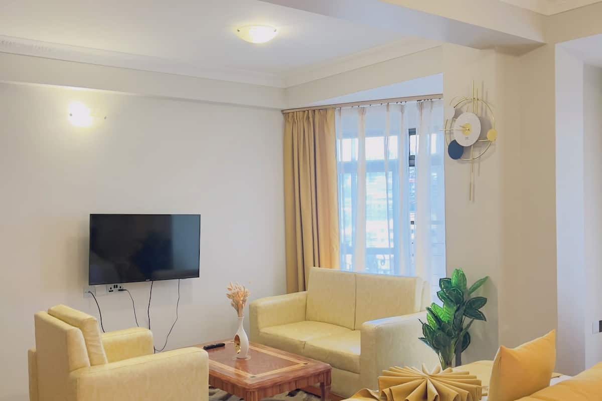 A hotel room with a bed, two sofas, a coffee table, a TV, and a window with curtains.