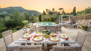 Un espace extérieur aménagé pour les repas, avec une piscine, des meubles en osier et une vue panoramique sur les collines et les arbres.