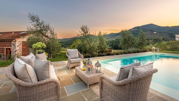 Un espace aménagé au bord de la piscine, avec des meubles en osier et une vue sur un paysage montagneux.
