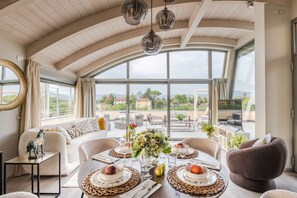 En rummelig balkon med spiseplads, store vinduer der giver udsigt over landskabet, og et højt hvælvet loft.