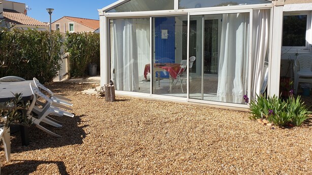 A covered patio area with a glass enclosure, a table, chairs, and a small garden.