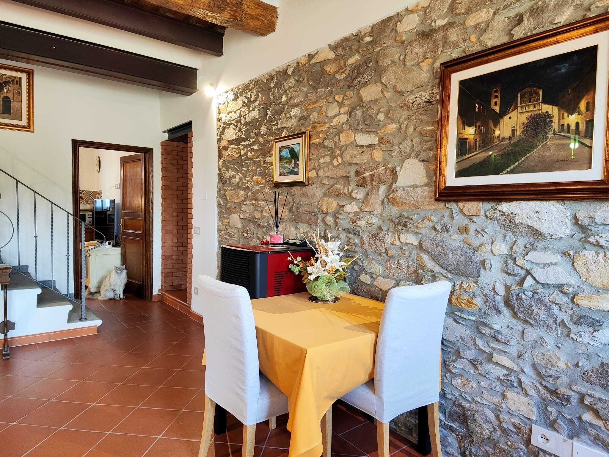 A dining area with a stone wall, a table with a yellow tablecloth, white chairs, and a framed picture.