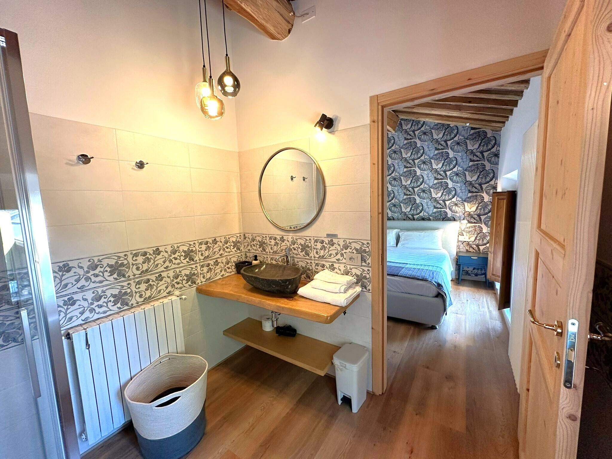 A bathroom with a wooden vanity, a round mirror, a vessel sink, and a towel rack.