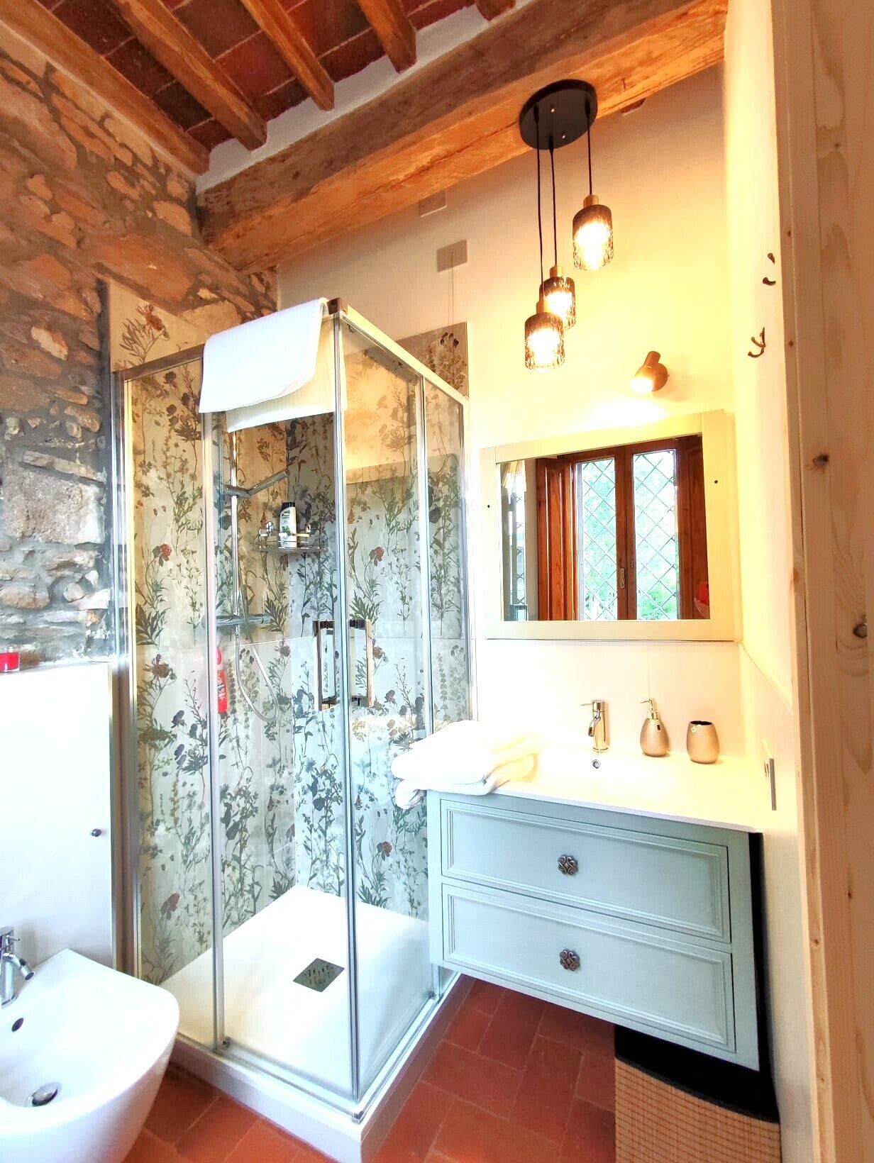 A bathroom with a glass shower enclosure, a white sink, a vanity with a mirror, and wooden beams on the ceiling.