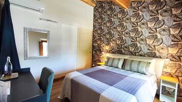A bedroom with a bed, a desk, a chair, a mirror, and a patterned wall.