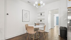A modern kitchen with a stainless steel refrigerator, a white dining table with four chairs, and a pendant light with multiple bulbs.