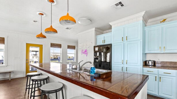 A kitchen with a wooden island, bar stools, light blue cabinets, and orange pendant lights. - Beach Walk Retreat, Game Room & King Bed (Bolivar Peninsula)