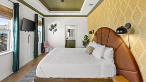 A bedroom with a bed, a ceiling fan, a TV, a mirror, and a wall-mounted lamp. - Beach Walk Retreat, Game Room & King Bed (Bolivar Peninsula)