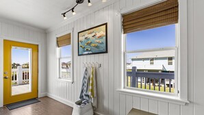 A room with white paneled walls, a yellow door, and large windows with blinds. - Beach Walk Retreat, Game Room & King Bed (Bolivar Peninsula)