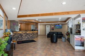 Un hall de hotel con mostrador de recepción, zona de estar y una pantalla de televisión.