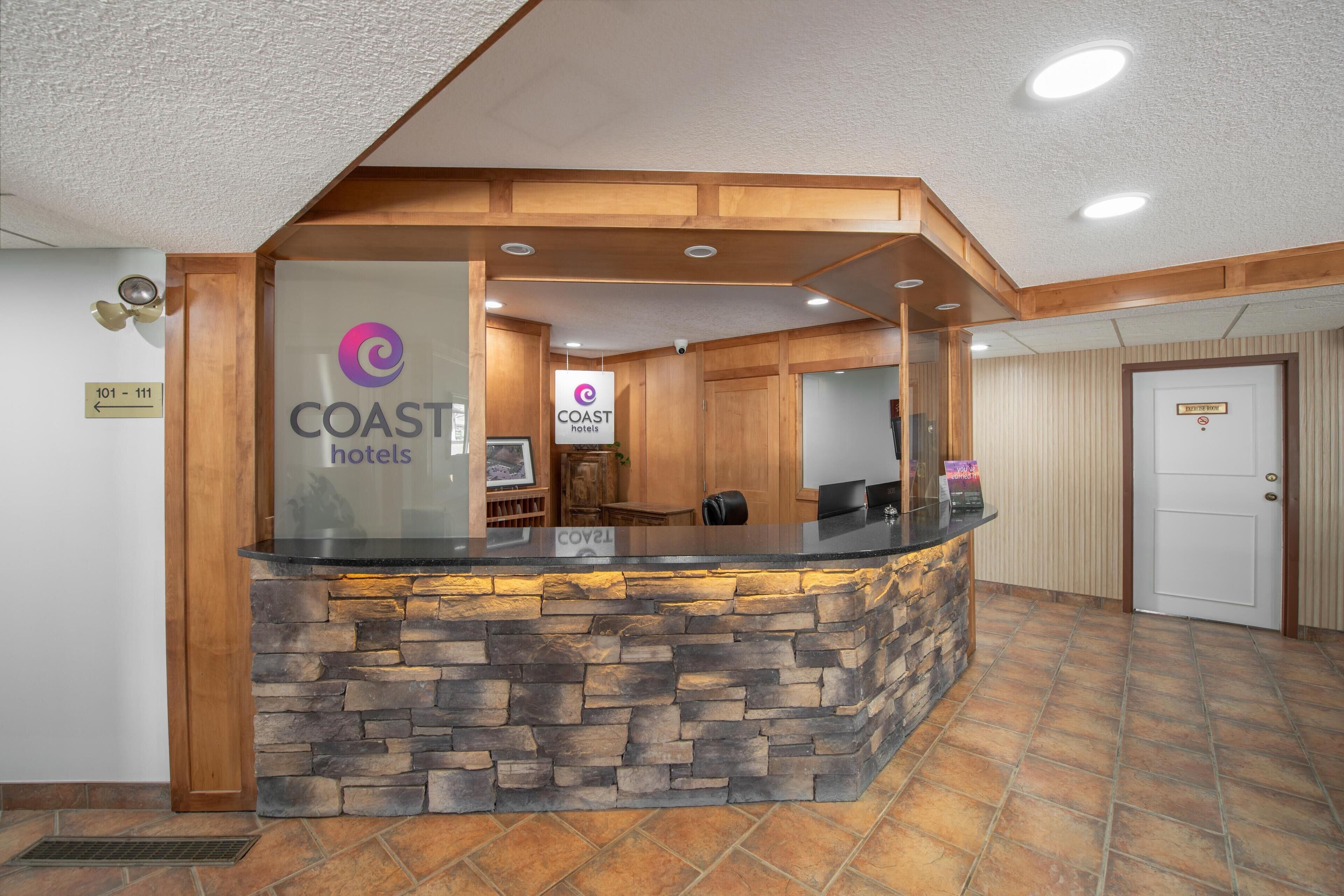 A reception area with a stone counter, wooden paneling, and a sign for COAST hotels.