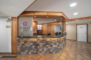 A reception area with a stone counter, wooden paneling, and a sign for COAST hotels. -  Coast Whitecourt Hotel (Whitecourt)