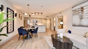 A modern living room with a white sofa, a coffee table, and a dining area with a table and chairs. - Luxury Suite, Full Kitchen, Heated Pool (Shanty Bay)