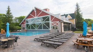 A poolside area with lounge chairs and umbrellas, a pool, and a building with large windows and a red facade. - Luxury Suite, Full Kitchen, Heated Pool (Shanty Bay)