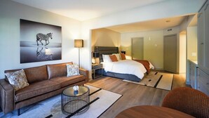 Una habitación de hotel moderna con una cama grande, un sofá, una mesita de centro y un cuadro en la pared.