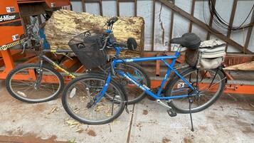 A blue bicycle with a basket and a bag attached to the rear, parked next to a wood chipper and a metal structure.
