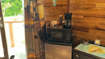 A room with wooden walls, a wooden floor, a microwave, a coffee maker, a small refrigerator, a cabinet with drawers, a map, and a sign that says "Endless Summer Bar".