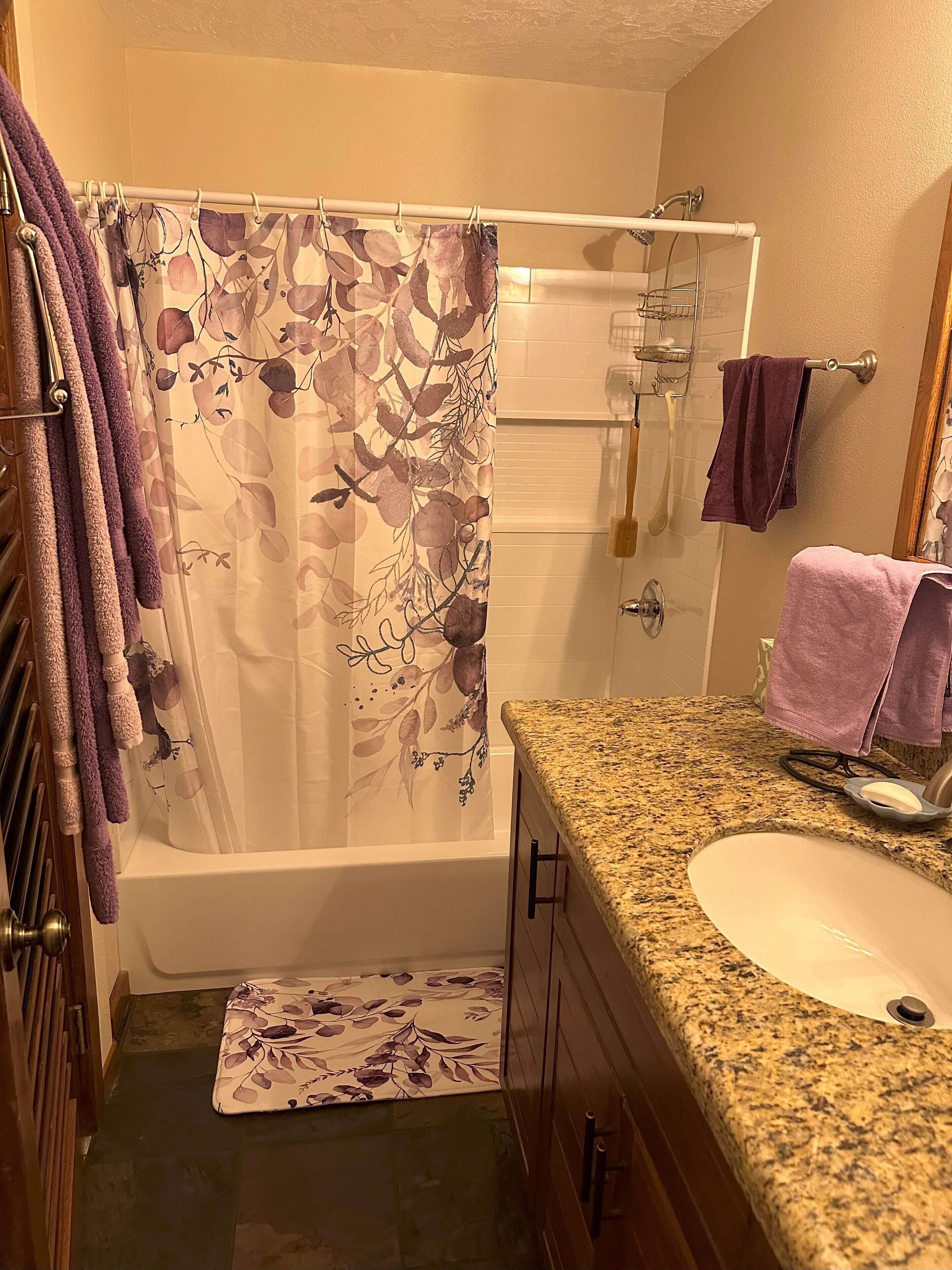 Ein Badezimmer mit Duschvorhang, Badewanne, einer Arbeitsplatte aus Granit, einem Waschbecken und einem Handtuchhalter.