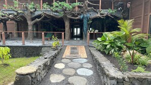 Un chemin de pierres menant à un bâtiment entouré d’une clôture en bois et agrémenté de verdure.