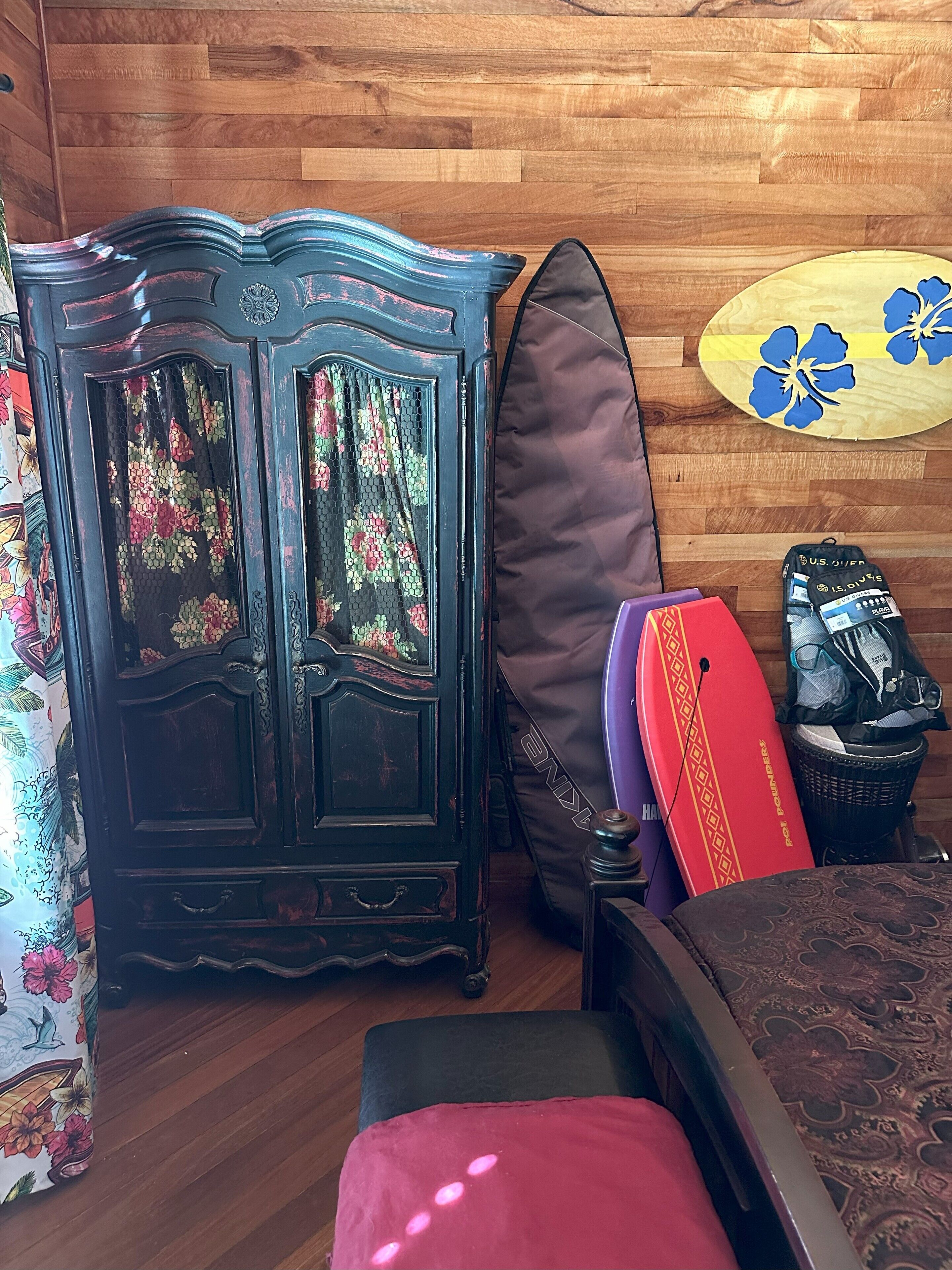 A room with a wooden cabinet, a surfboard, a bag, and a bed.