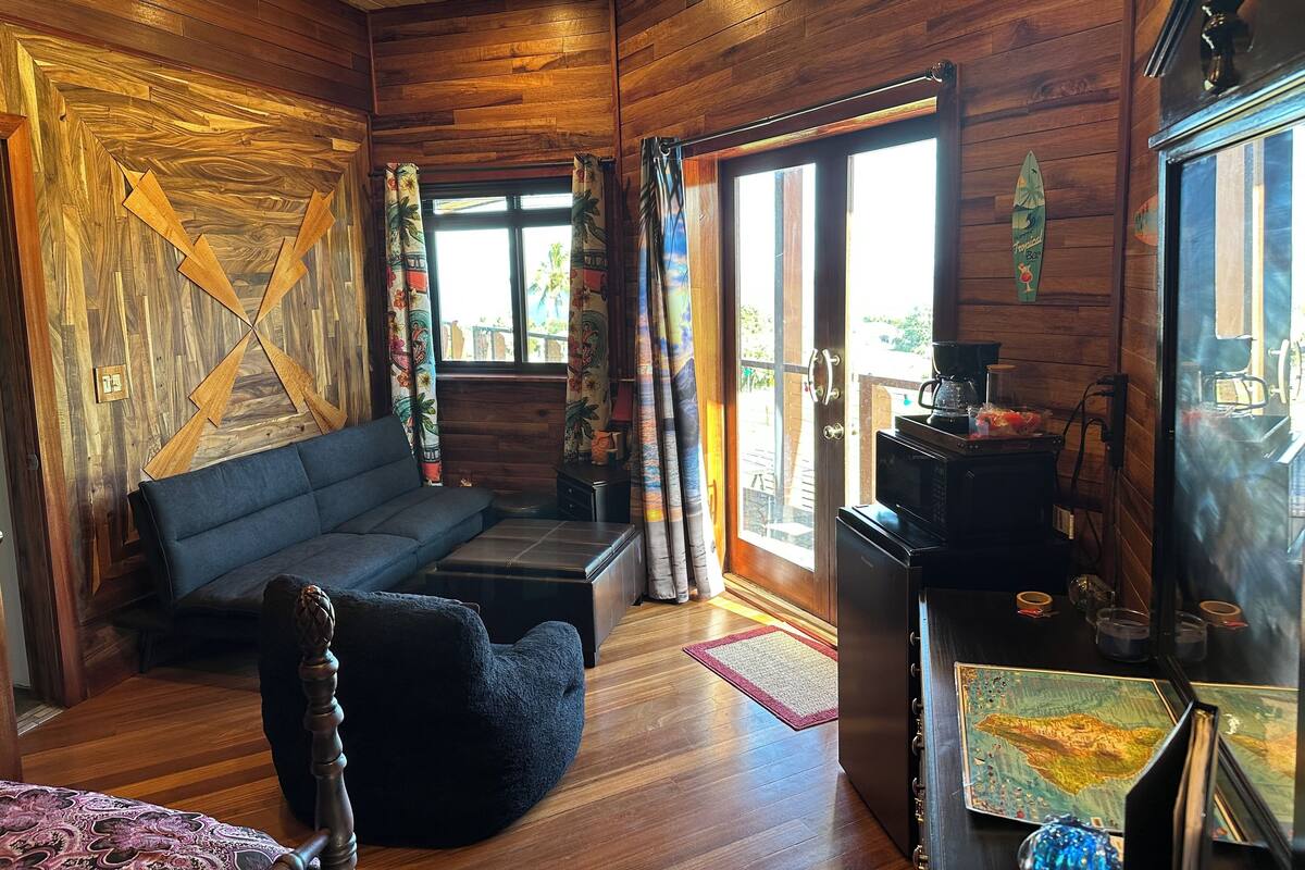 A cozy cabin interior with wooden walls, a sofa, a small table with a coffee maker, and a view through the door.