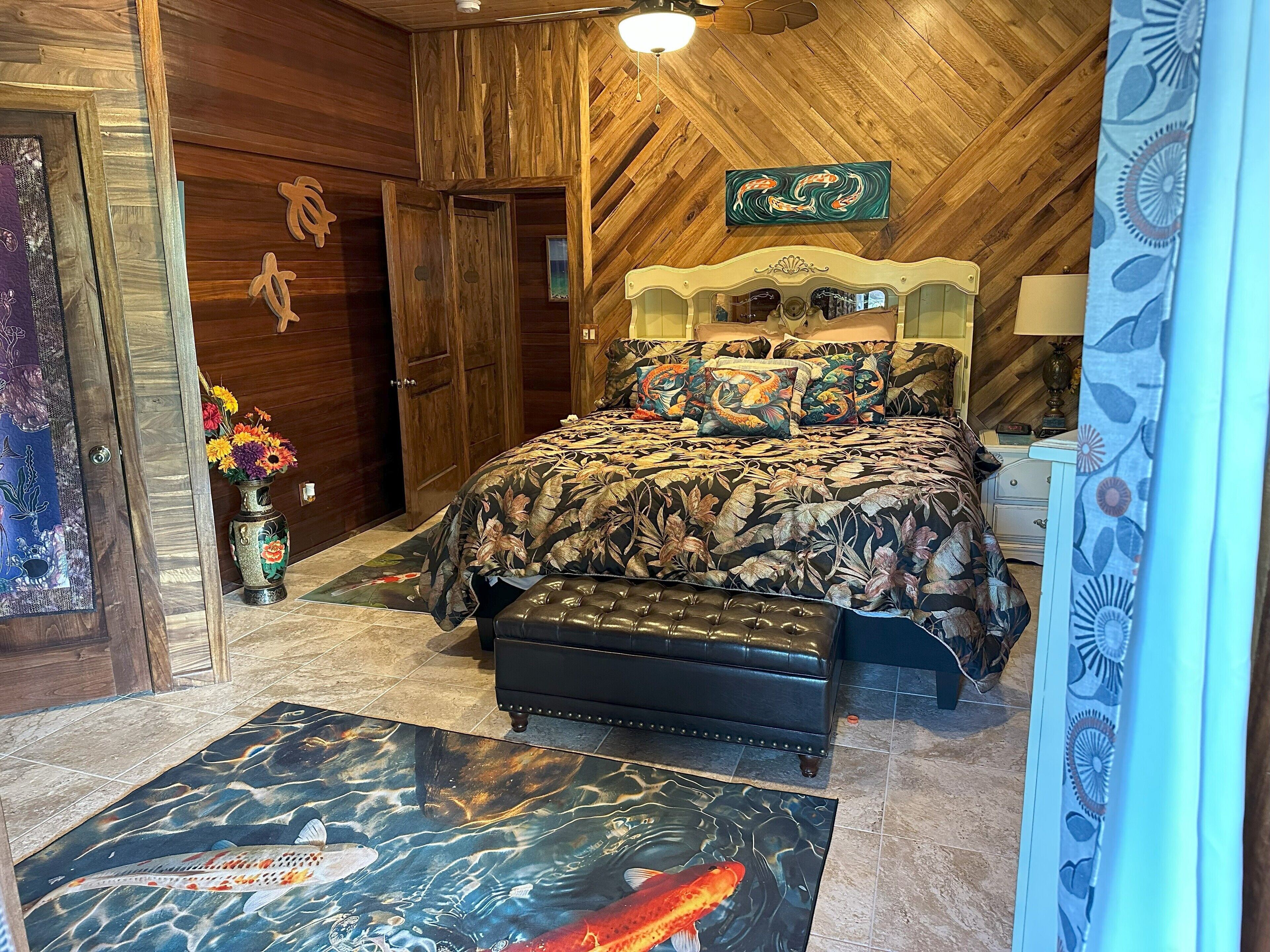Een slaapkamer met een houten plafond, een bed met bloemenbeddengoed, een nachtkastje en een vaas met bloemen.