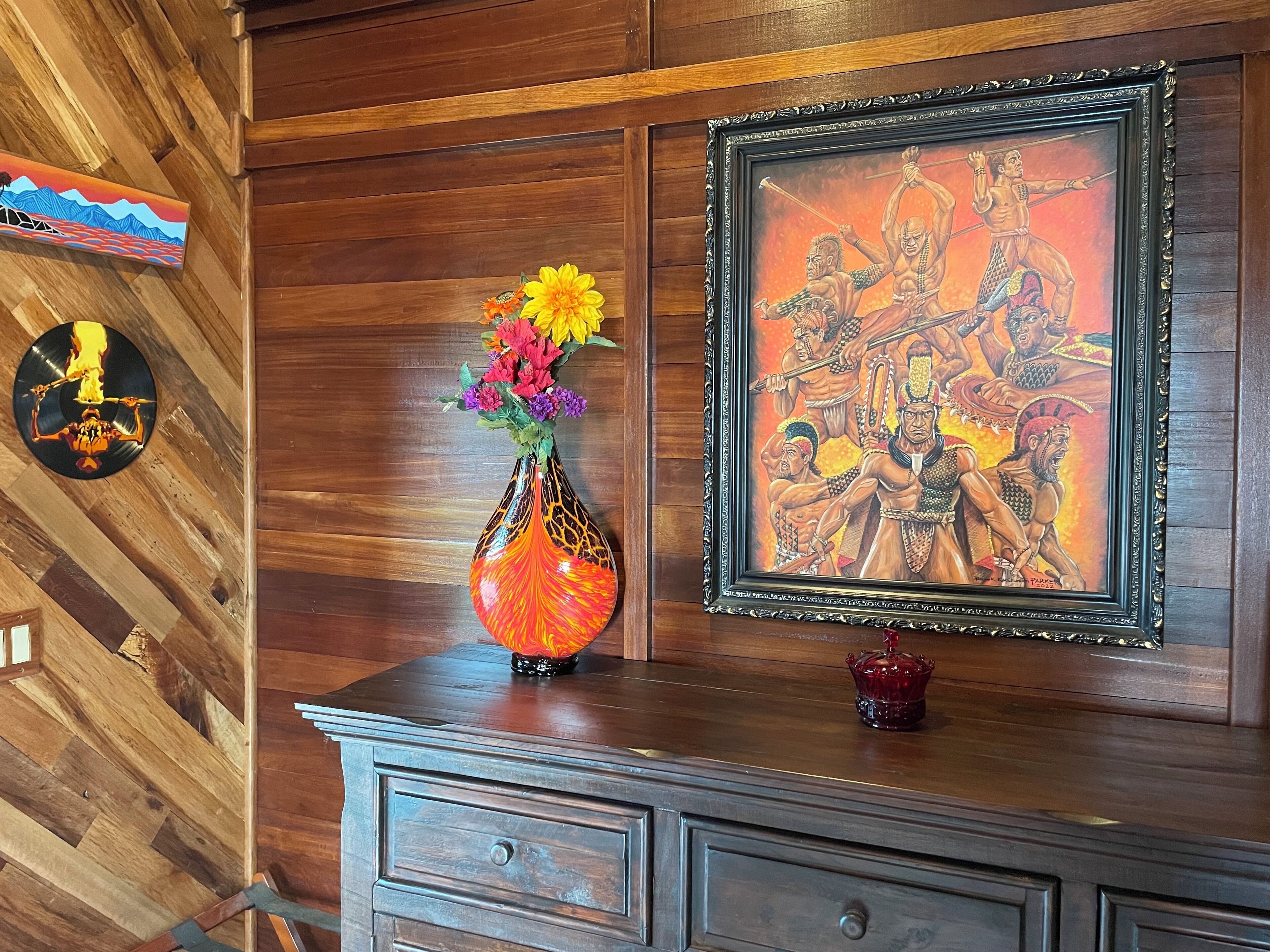 A wooden wall with a framed painting, a vase with flowers, and a vinyl record on the wall.
