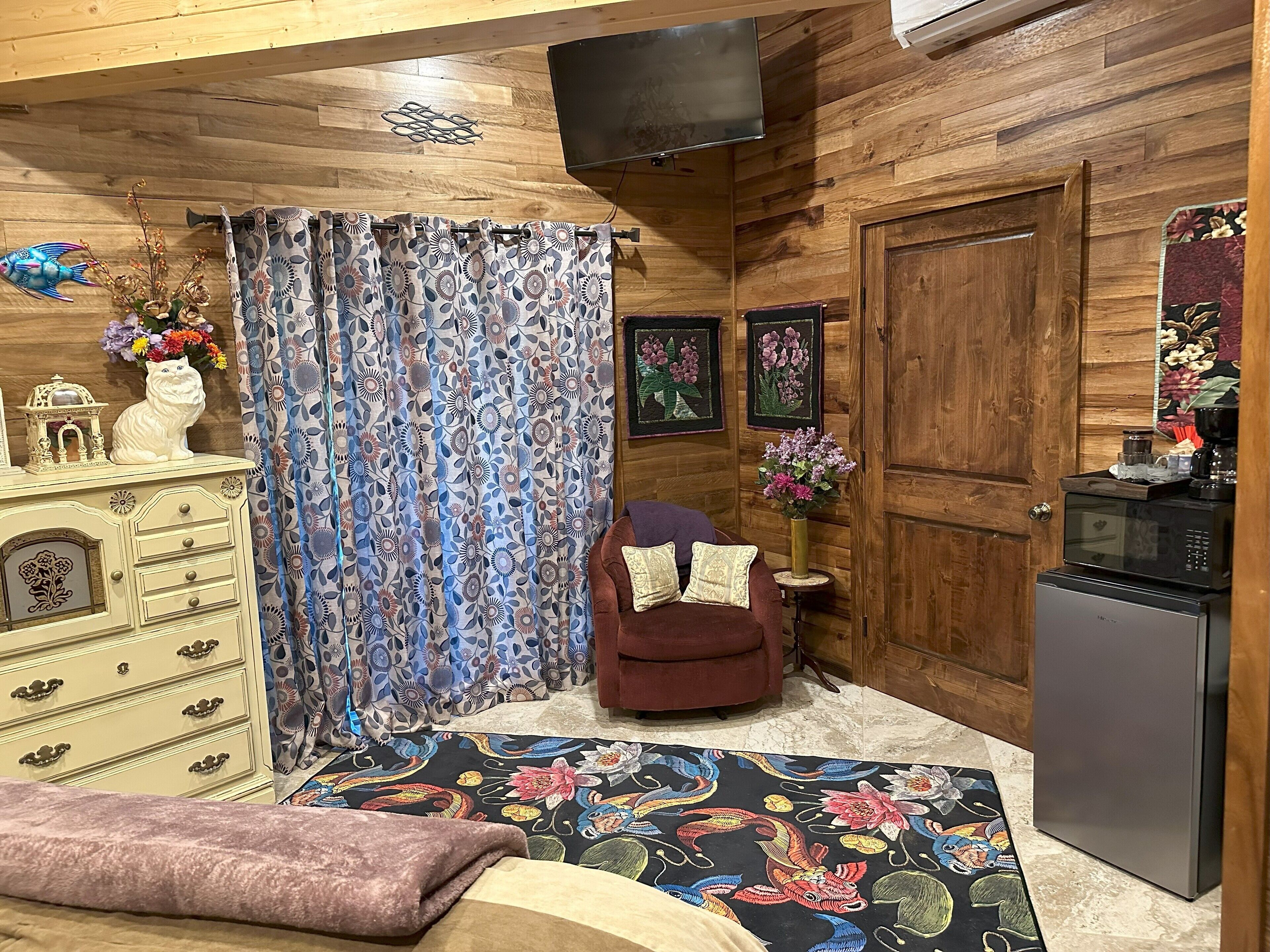A cozy room with a wooden ceiling, a patterned curtain, a small sofa, a decorative cabinet, and a microwave.