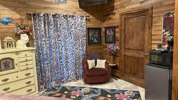 A cozy room with a wooden ceiling, a patterned curtain, a small sofa, a decorative cabinet, and a microwave.