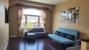 A living room with a sofa, a blue couch, and a television on the wall. - Big house for the big family! 6 bedrooms and 3.5 bathrooms.  (Kitchener)