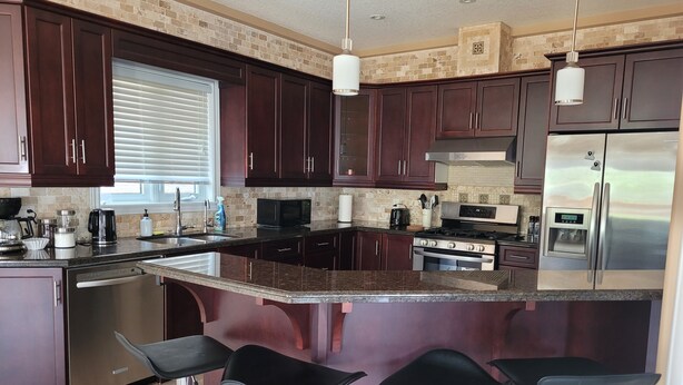 A modern kitchen with dark wood cabinets, a stainless steel refrigerator, a built-in oven, and a large island with bar stools. - Big house for the big family! 6 bedrooms and 3.5 bathrooms.  (Kitchener)