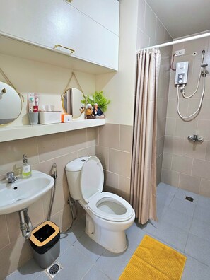 Bathroom features a white toilet, sink, and trash bin, along with a handheld showerhead and a potted plant.